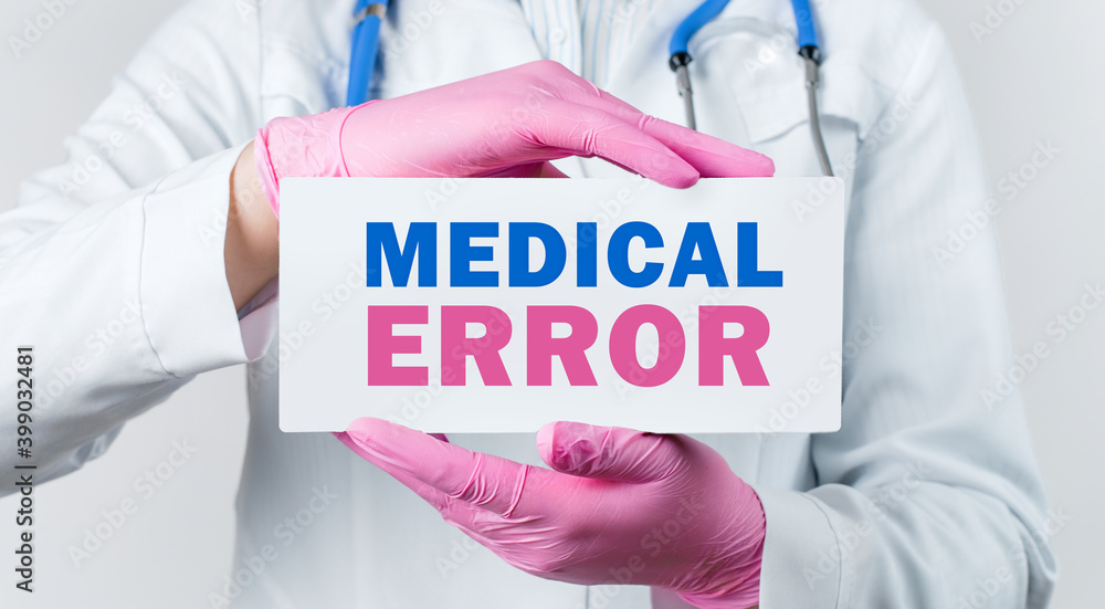 Cropped view of female doctor in a white coat and pink sterile gloves holding a card with words - medical error Cropped view of female doctor in a white coat and pink sterile gloves holding a card with words - medical error