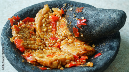 Penyet tempeh with chili sauce in a stone mortar. Focus selected