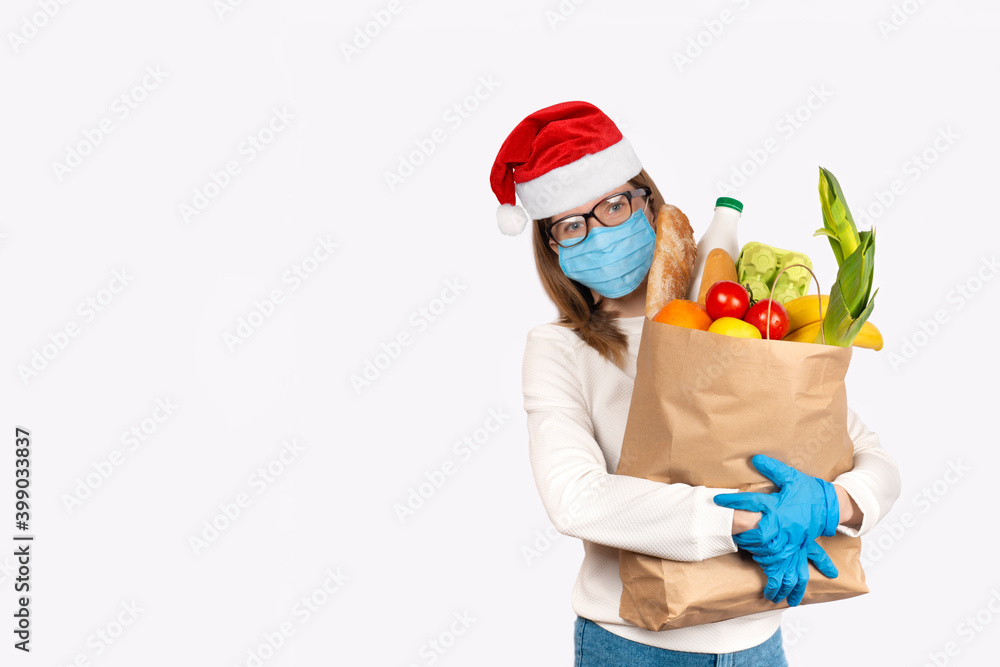 Young woman in disposable gloves and Santa hat holding Box with food ingredients Young woman in disposable gloves and Santa hat holding Box with food ingredients