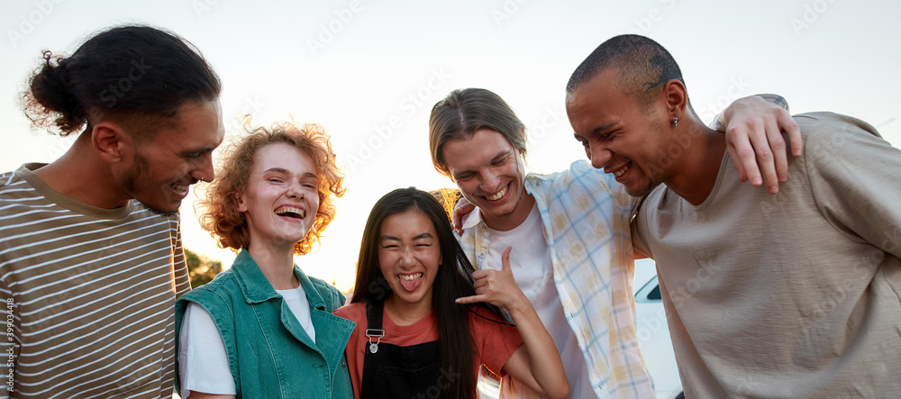Obraz premium Five casually dressed friends of different nationalities having a good time together outside laughing and smiling hugging each other