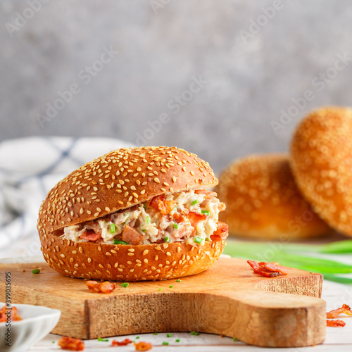 Delicious sesame bun sandwich with chicken salad, fried bacon, green onions, cheese with ranch sauce. Lunch or dinner for gourmets. Selective focus