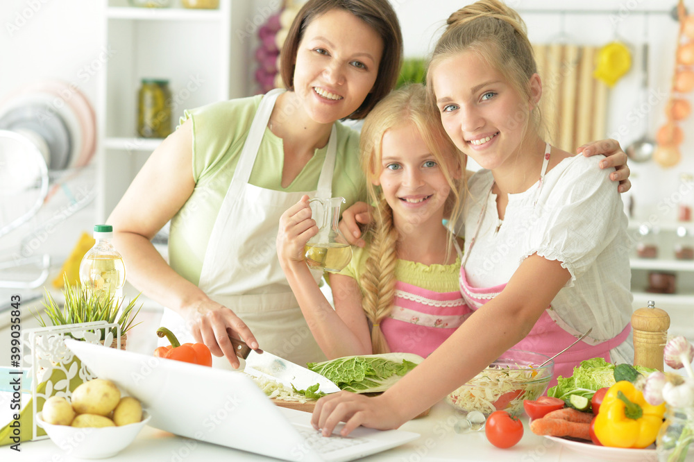 Cute girls with mother preparing delicious fresh salad in kitchen