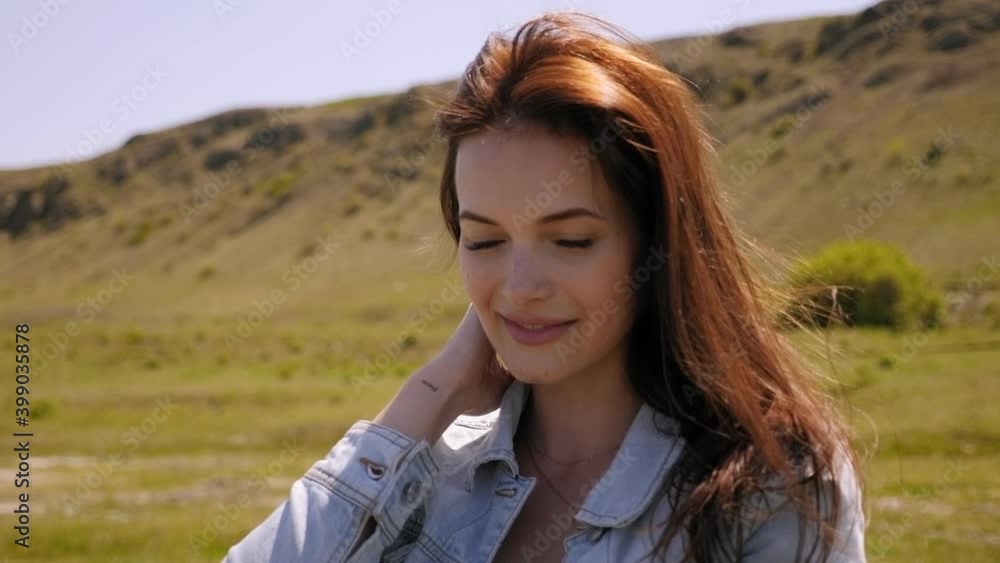 Portrait of a young beautiful girl with dark flowing hair in a field against the background of mountains, she smiles and looks at the camera. Portrait of a young beautiful girl with dark flowing hair in a field against the background of mountains, she smiles and looks at the camera.