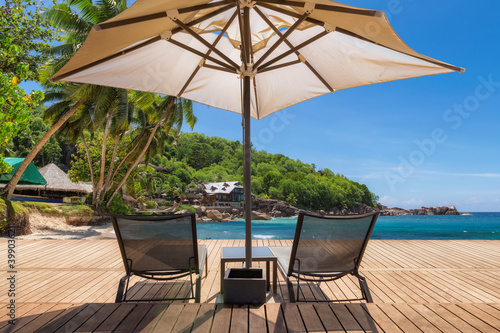 Гmbrella and deckchairs on tropical Sunny beach with wooden floor, palm trees and the turquoise sea on Caribbean island 