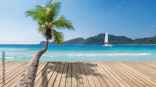 Sunny beach with wooden floor, palm trees and a sailing boat in the turquoise sea on Paradise island.