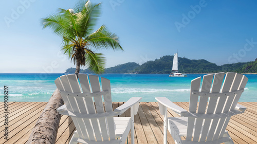 Sunny Caribbean beach with white chairs on wooden floor  palm trees and a sailing boat in the turquoise sea on Paradise island.