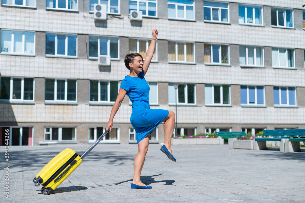 Happy woman walking down the street holding yellow suitcase with wheels Happy woman walking down the street holding yellow suitcase with wheels