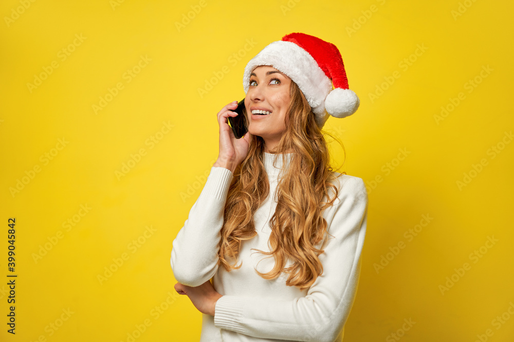 Woman christmas Santa Hat yellow studio background with smartphone in hand Woman christmas Santa Hat yellow studio background with smartphone in hand