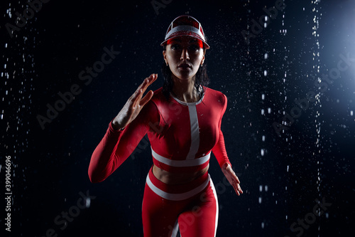 Beautiful young girl in sportswear runing in aqua studio. Drops of water spread about her fitness body. The perfect figure on the background of water splashes. Bad weather for sport © Andrii
