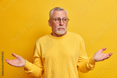 Fotografie Portrait of puzzled hesitant bearded mature man spreads palms and faces difficul