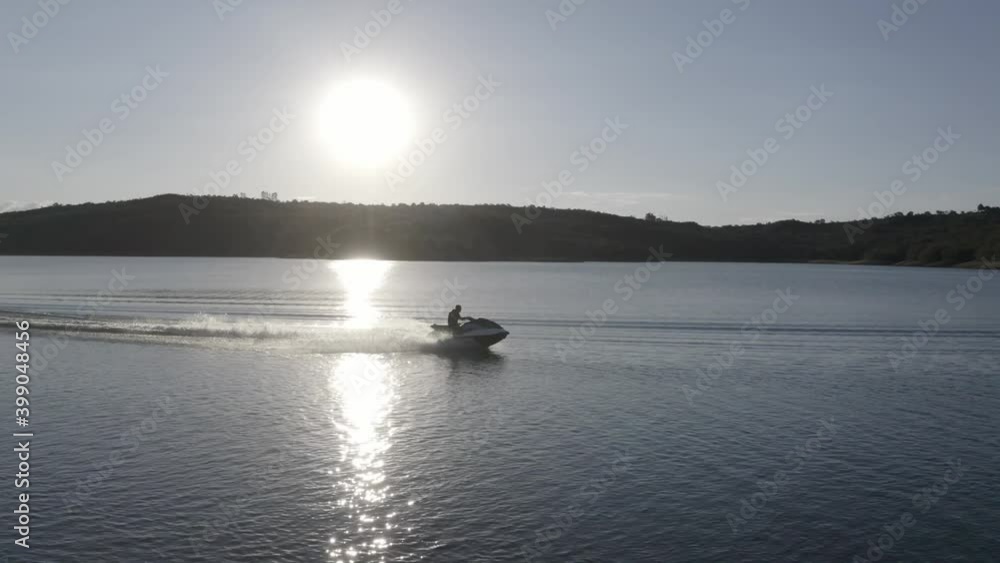 Silhouette of a jet ski speeding over the surface of a large lake with the sun reflecting off the water - aerial view Silhouette of a jet ski speeding over the surface of a large lake with the sun reflecting off the water - aerial view