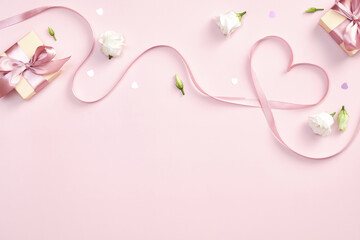 Ribbon in shape of heart with gift boxes and rose flowers on pink background. Happy Valentines day, Mothers day, birthday concept. Romantic flat lay composition.