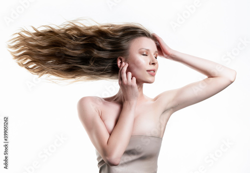 A beautiful girl with large breasts and naked shoulders sensually touches her face with hands, while her long hair flutters horizontally to the side. Isolated on white. Advertising, commercial design