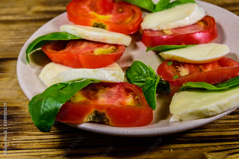 Plate with caprese salad (italian salad with cherry tomatoes, mozzarella cheese and basil leaves) on wooden table Plate with caprese salad (italian salad with cherry tomatoes, mozzarella cheese and basil leaves) on wooden table