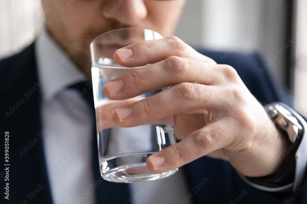 Close up cropped confident businessman drinking enjoying fresh pure mineral water, young employee holding glass, preventing dehydration, skin and health care, healthy lifestyle habit concept Close up cropped confident businessman drinking enjoying fresh pure mineral water, young employee holding glass, preventing dehydration, skin and health care, healthy lifestyle habit concept