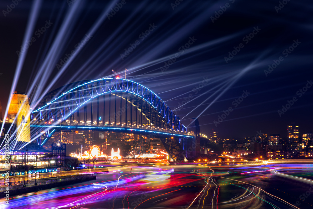 Fototapeta premium Sydney Harbour Bridge and bay at night with lights beaming from the top for Vivid Festival, and boat lights in the bay.