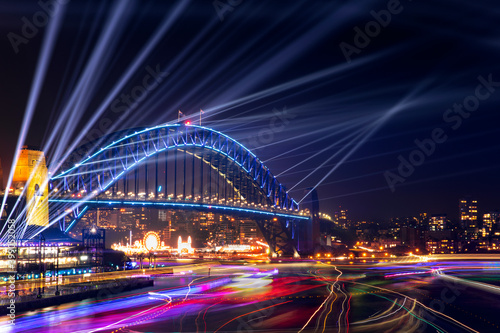 Sydney Harbour Bridge and bay at night with lights beaming from the top for Vivid Festival, and boat lights in the bay. © Bostock