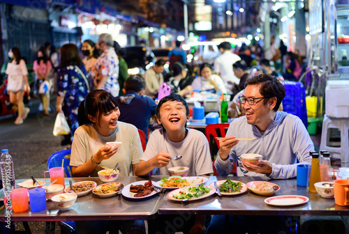 Asian family enjoy eating food on street food restaurant with crowd of people at Yaowarat road, Bangkok photo