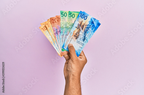 Hispanic hand holding swiss franc banknotes over isolated pink background. photo