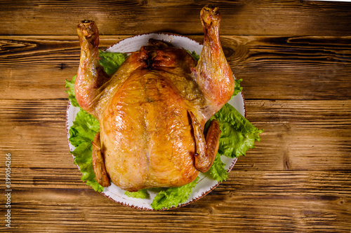 Plate with roasted whole chicken and lettuce leaves on a wooden table. Top view