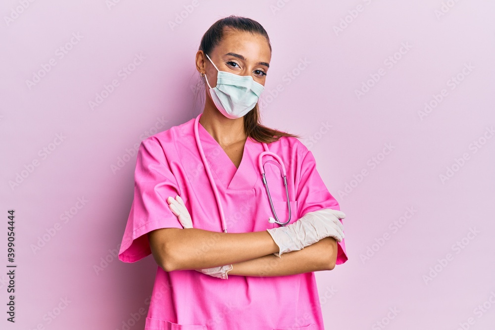Young hispanic woman wearing doctor uniform and medical mask happy face smiling with crossed arms looking at the camera. positive person. Young hispanic woman wearing doctor uniform and medical mask happy face smiling with crossed arms looking at the camera. positive person.