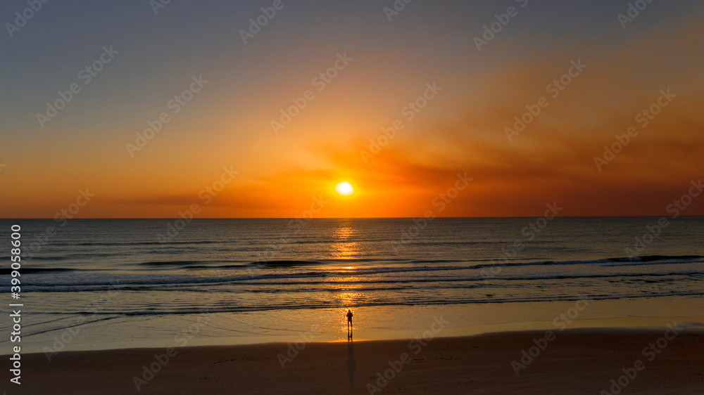 Person standing on beach at sunrise	