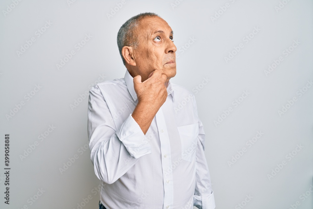 Handsome senior man wearing casual white shirt with hand on chin thinking about question, pensive expression. smiling and thoughtful face. doubt concept. Handsome senior man wearing casual white shirt with hand on chin thinking about question, pensive expression. smiling and thoughtful face. doubt concept.