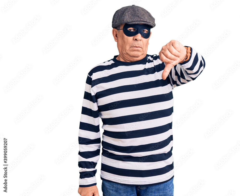 Senior handsome man wearing burglar mask and t-shirt looking unhappy and angry showing rejection and negative with thumbs down gesture. bad expression. Senior handsome man wearing burglar mask and t-shirt looking unhappy and angry showing rejection and negative with thumbs down gesture. bad expression.