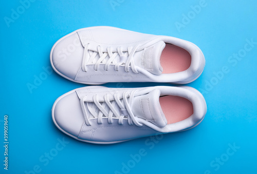 Pair of stylish sport shoes on blue background. Top view of white sneakers on color background