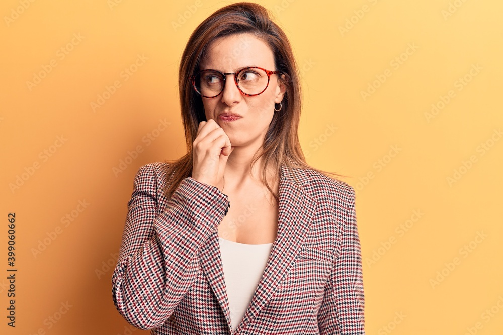 Young beautiful woman wearing business clothes and glasses serious face thinking about question with hand on chin, thoughtful about confusing idea Young beautiful woman wearing business clothes and glasses serious face thinking about question with hand on chin, thoughtful about confusing idea