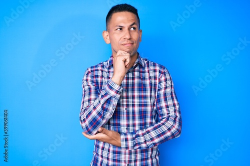 Young handsome latin man wearing casual clothes with hand on chin thinking about question, pensive expression. smiling with thoughtful face. doubt concept.