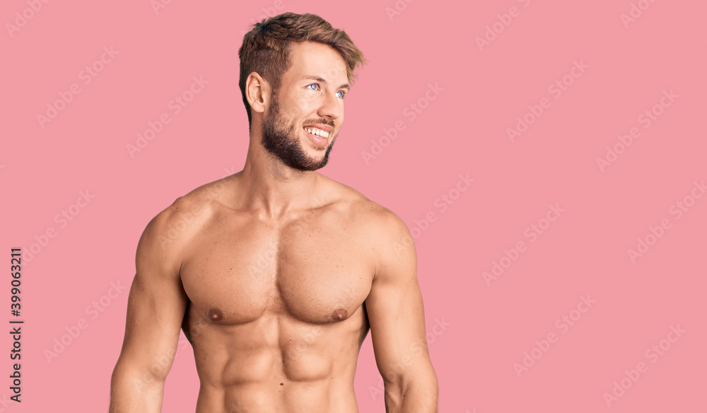 Fototapeta premium Young caucasian man standing shirtless looking away to side with smile on face, natural expression. laughing confident.