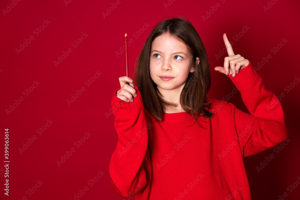 Obraz premium beautiful young school girl with red pencil and red sweater is standing in front of a red background