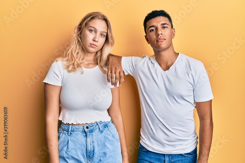 Young interracial couple wearing casual white tshirt relaxed with serious expression on face. simple and natural looking at the camera.