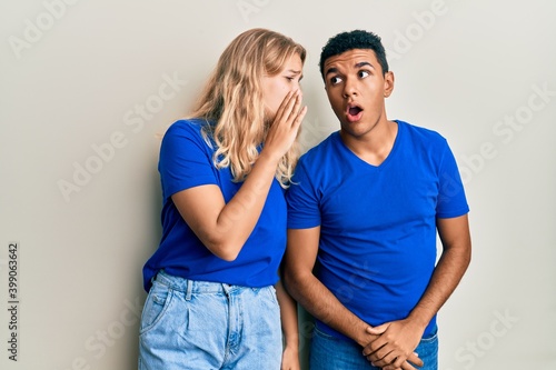 Young interracial couple wearing casual clothes hand on mouth telling secret rumor, whispering malicious talk conversation