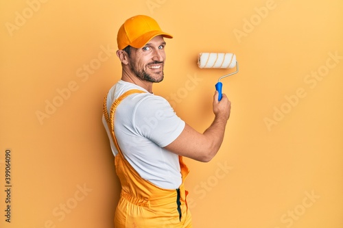 Young caucasian painter smiling happy painting wall using roller.