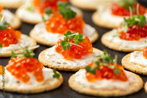 Salmon caviar and soft cheese savory crackers with sesame and poppy seeds served on black slate board