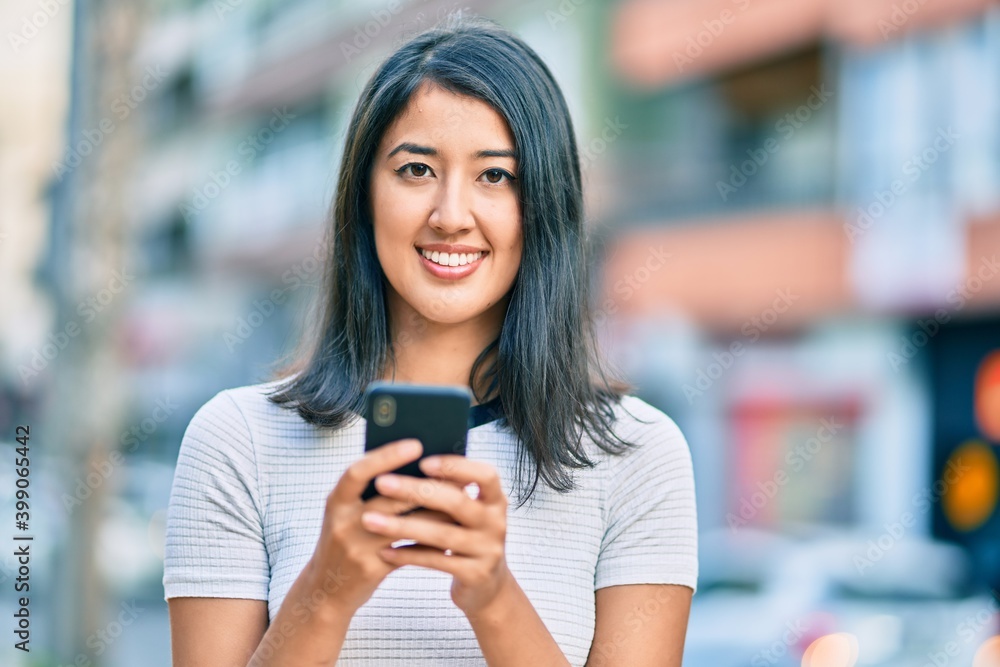 Fototapeta premium Young hispanic woman smiling happy using smartphone at the city.
