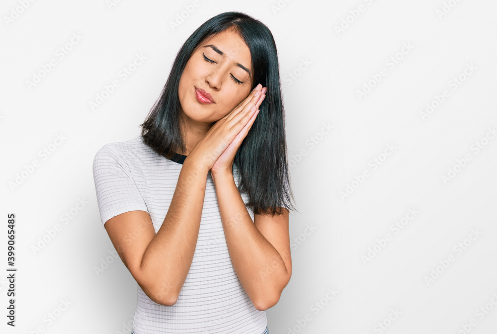 Beautiful asian young woman wearing casual white t shirt sleeping tired dreaming and posing with hands together while smiling with closed eyes. Beautiful asian young woman wearing casual white t shirt sleeping tired dreaming and posing with hands together while smiling with closed eyes.