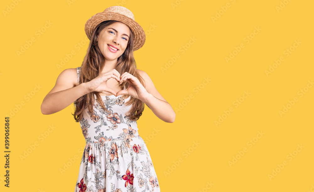 Beautiful caucasian young woman wearing summer hat smiling in love doing heart symbol shape with hands. romantic concept. Beautiful caucasian young woman wearing summer hat smiling in love doing heart symbol shape with hands. romantic concept.