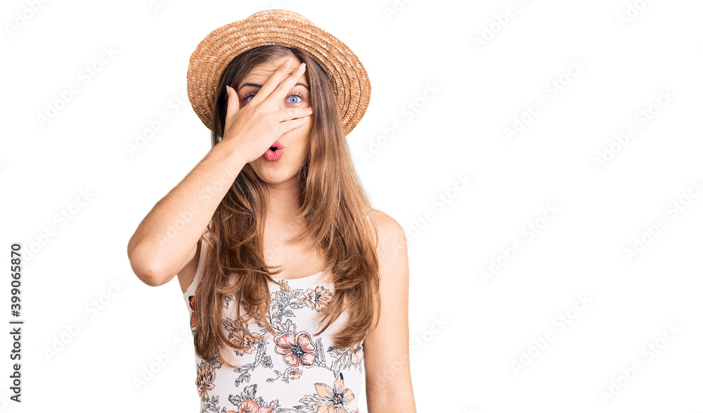 Beautiful caucasian young woman wearing summer hat peeking in shock covering face and eyes with hand, looking through fingers with embarrassed expression. Beautiful caucasian young woman wearing summer hat peeking in shock covering face and eyes with hand, looking through fingers with embarrassed expression.