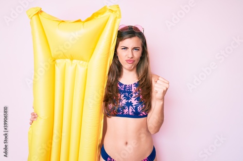 Beautiful young caucasian woman wearing bikini and holding summer matress float annoyed and frustrated shouting with anger, yelling crazy with anger and hand raised © Krakenimages.com