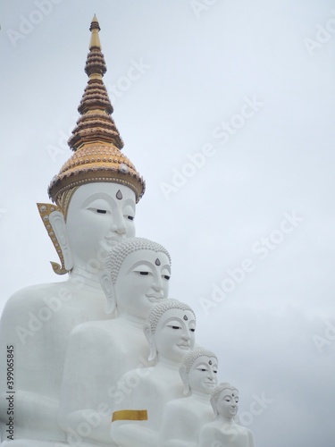 A temple in Thailand that is lined with four white Buddha statues and a light blue sky.