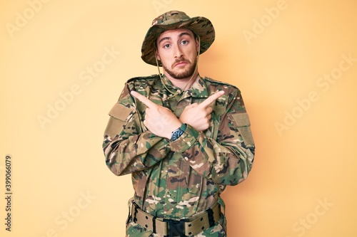 Young caucasian man wearing camouflage army uniform pointing to both sides with fingers, different direction disagree