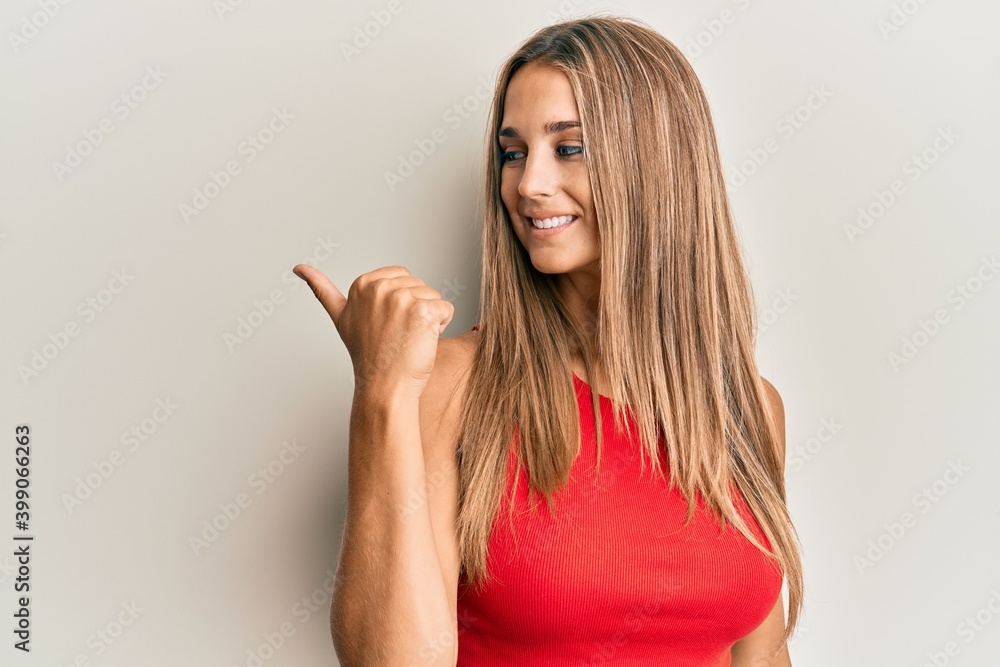 Fototapeta premium Young blonde woman wearing casual clothes smiling with happy face looking and pointing to the side with thumb up.