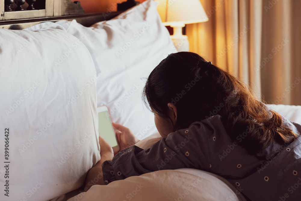 young girl reading novel on smartphone and lying on the bed at home
