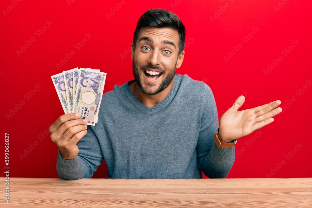 Handsome hispanic man holding japanese yen banknotes celebrating achievement with happy smile and winner expression with raised hand Handsome hispanic man holding japanese yen banknotes celebrating achievement with happy smile and winner expression with raised hand