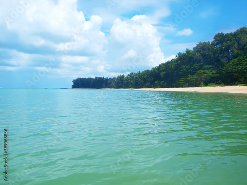 Panoramic view from the sea to the green cliff covered by rainforest, land, sandy coast. Turquoise color calm water and blue sky with beautiful clouds. Seascape and tropical nature. Thailand, Phuket  © Oxana
