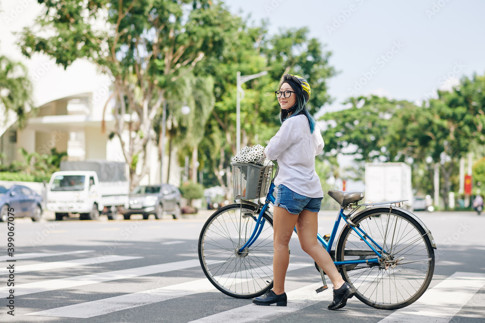 Obraz premium Smiling pretty Chinese woman in helmet walking next to her bicycle when crossing road