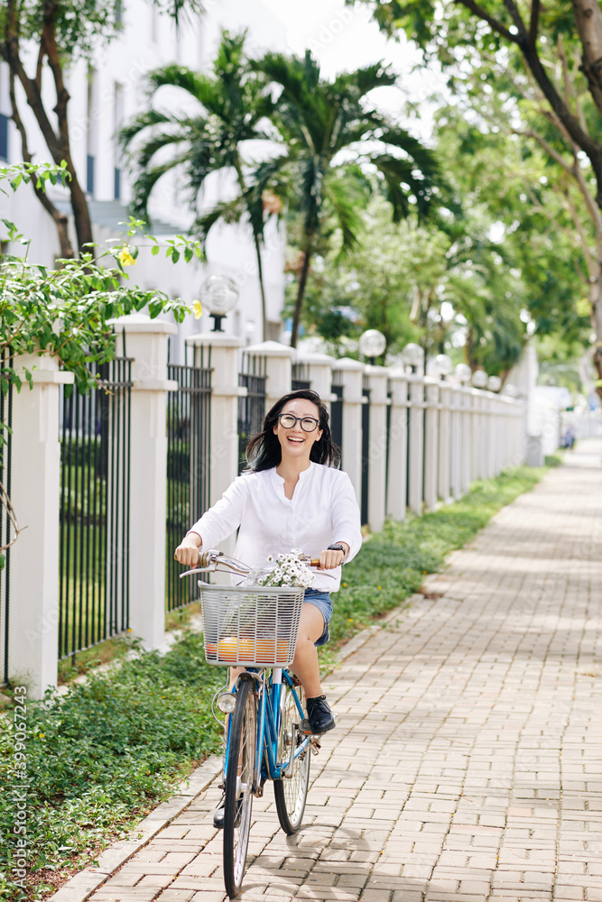 Happy young Chinese woman riding on bicycle down city street